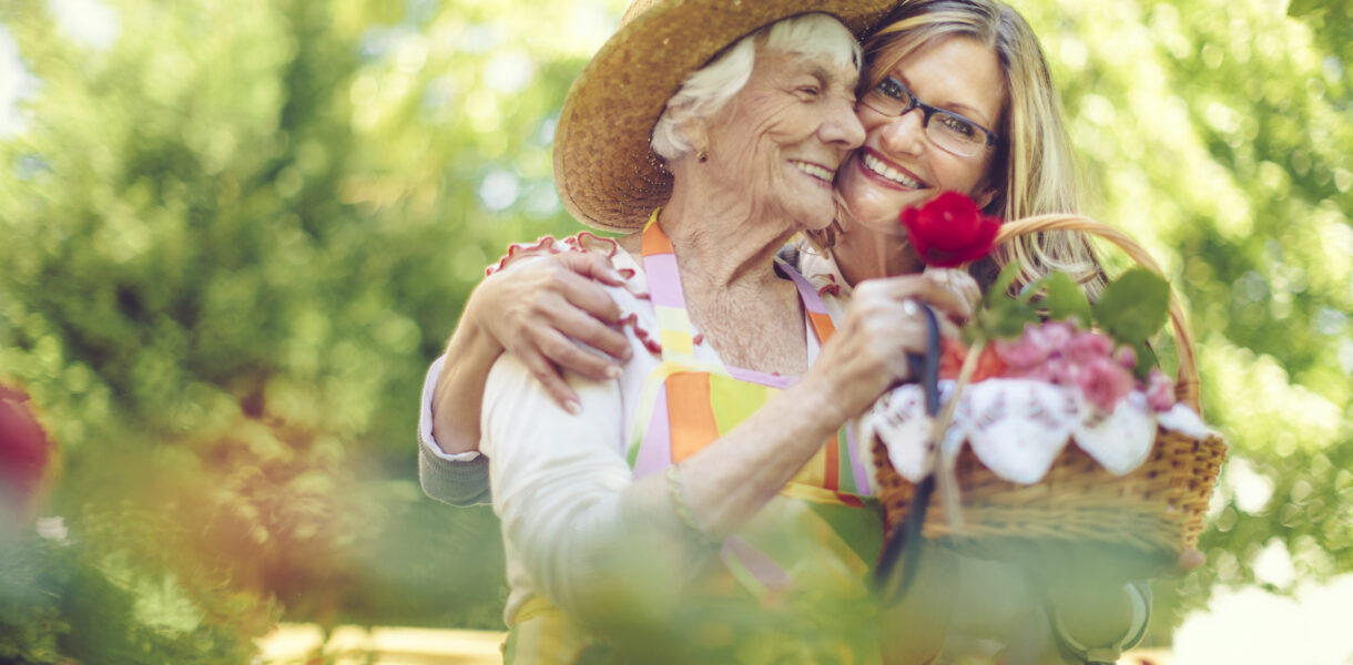 A memory care patient and a young woman hugging while holding a basket of flowers