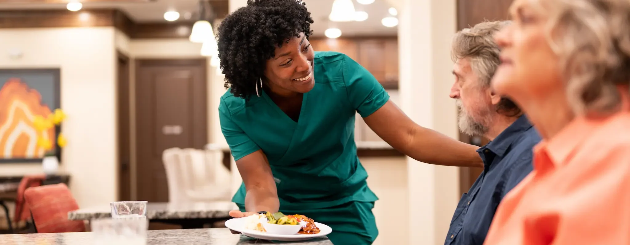 A staff member at Avalon Memory Care smiles while serving a plate of food to memory care residents.
