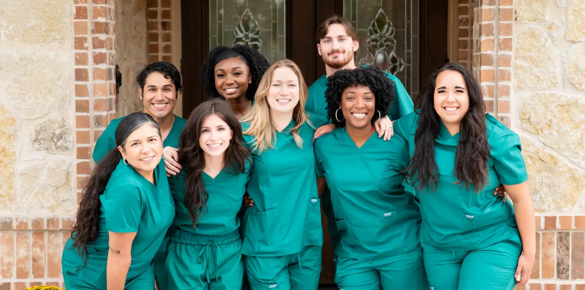 A group of smiling Avalon Memory Care staff members wearing green scrub uniforms.